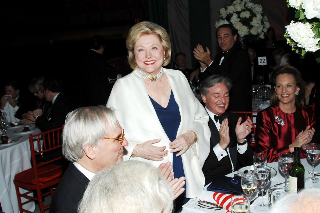 Barbara Taylor Bradford stood up smiling at a dinner party wearing a white shawl and navy dress