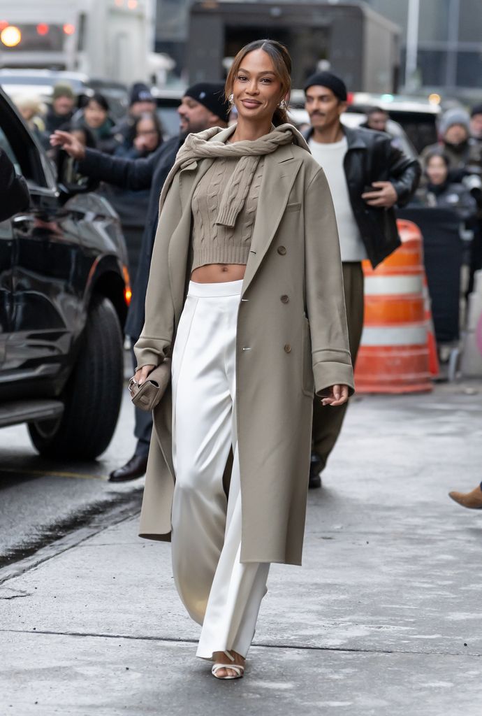 Joan Smalls porte un pantalon blanc et une veste-pull grège assortie ainsi qu'un deuxième pull noué autour du cou.