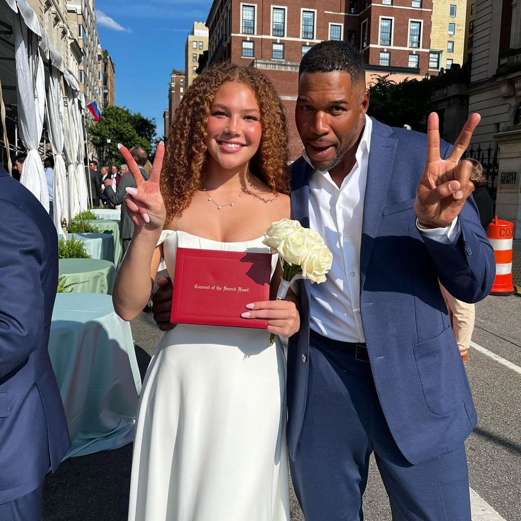 Michael Strahan in a blue suit making a peace sign with daughter Isabella