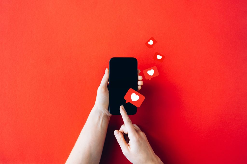 Hands Holding Smartphone with Social Media Love Icons on Vibrant Red Background