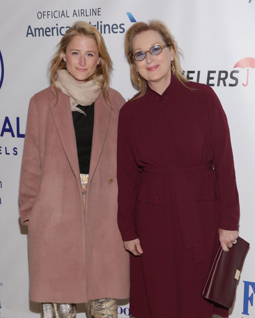Mamie Gummer in a pink trench coat (L) and Meryl Streep in a red coat posing 