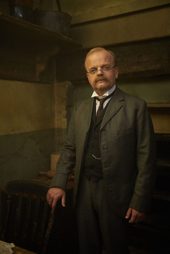A man in period dress leans on a chair