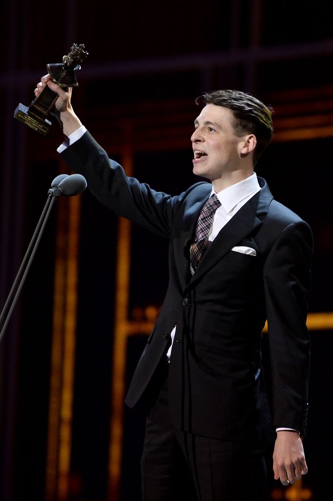A photo of a man in a black suit holding an award 