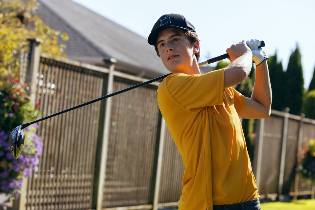 young teen in yellow shirt swinging golf club in garden