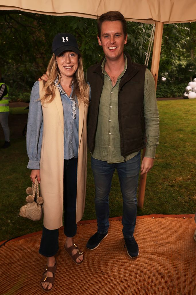 Jemima Cadbury Tollemache and David Tollemache pose under a garden tent, with her in a frilled blouse, wide-leg jeans, sandals and a wool vest, and him in a green shirt and quilted gilet—quintessential countryside-meets-city style at Cadogan Place Gardens.