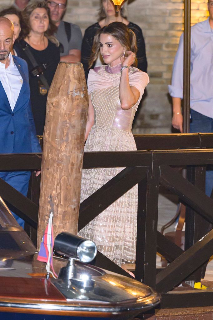 Queen Rania porte une robe rose blush avec une jupe ornée à paillettes et un décolleté drapé en satin, accessoirisé avec un chignon doux et des bijoux en diamant.