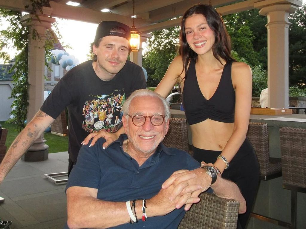 Nicola Peltz and Brooklyn Beckham standing behind Nelson Peltz