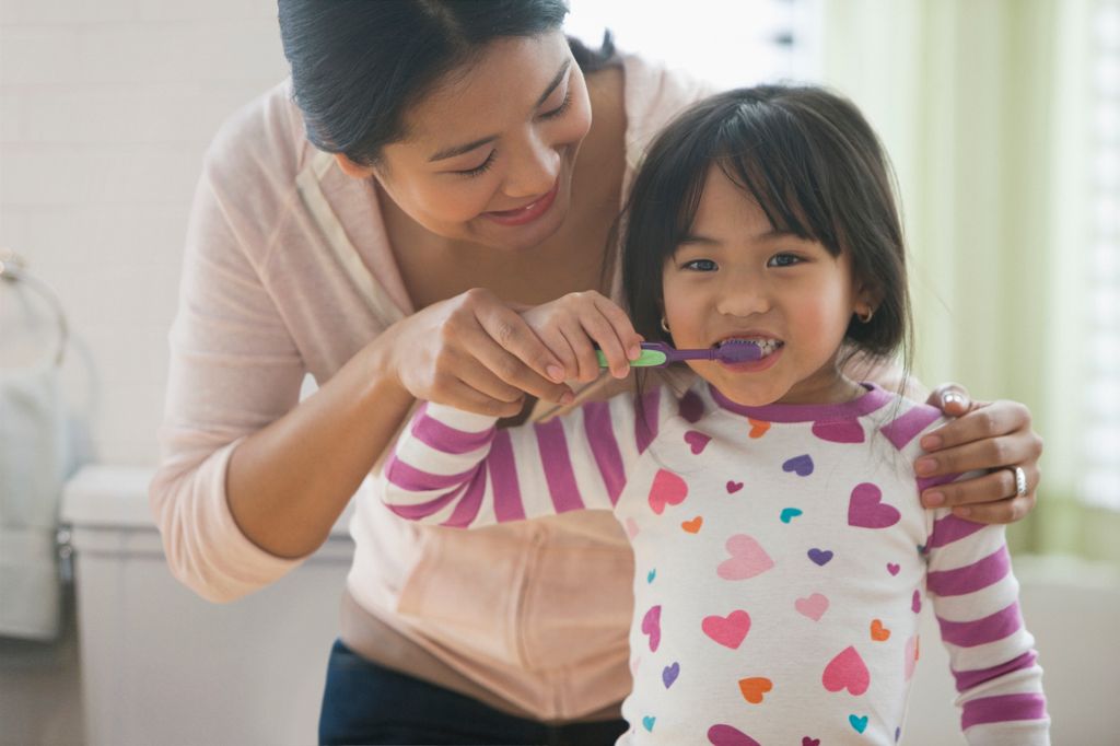 A mother helping her young child to brush her teeth