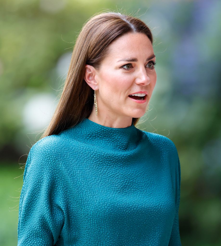Catherine in teal dress shoulders up looking shocked