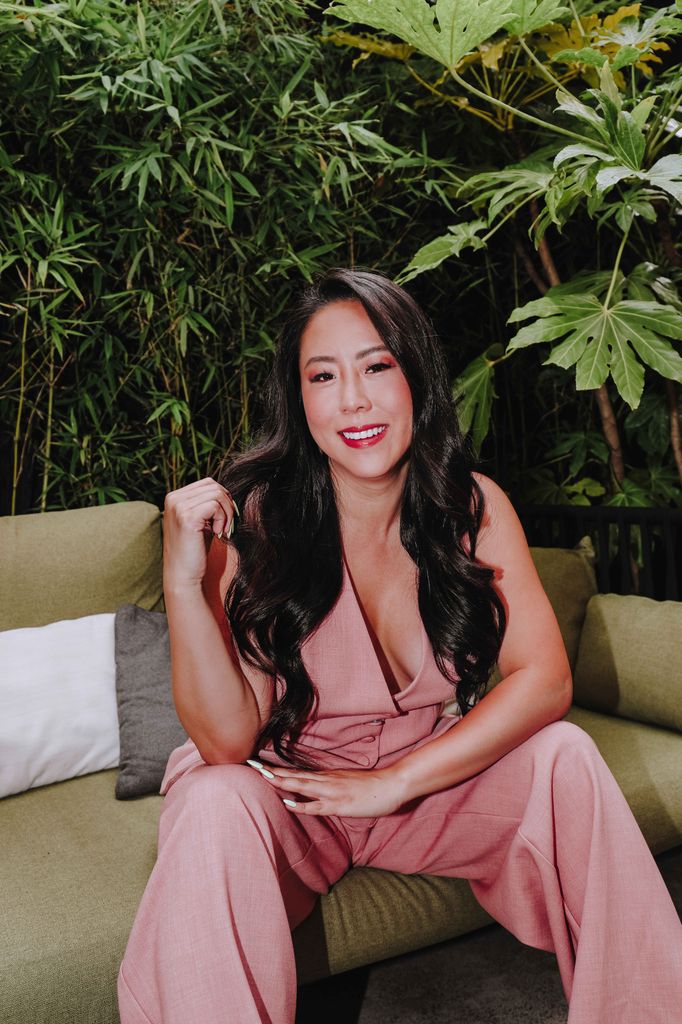 woman with long dark hair sitting on a sofa in a green jumpsuit