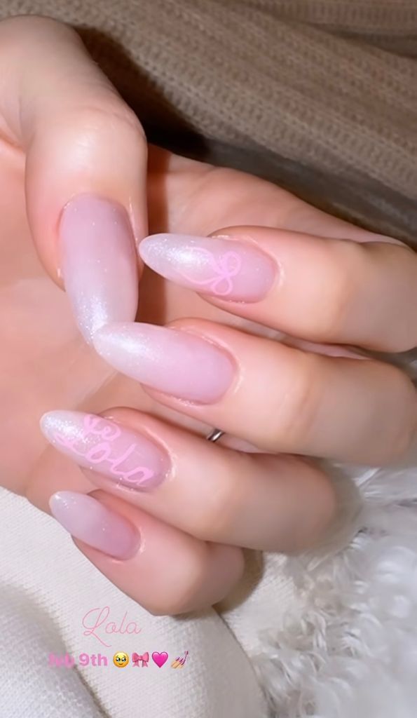 Nicola Peltz's pink shimmery nails with a bow on one finger and the word "Lola" on another 