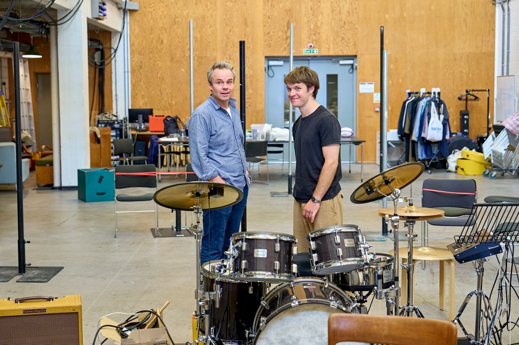 Two men stand beside a drum kit