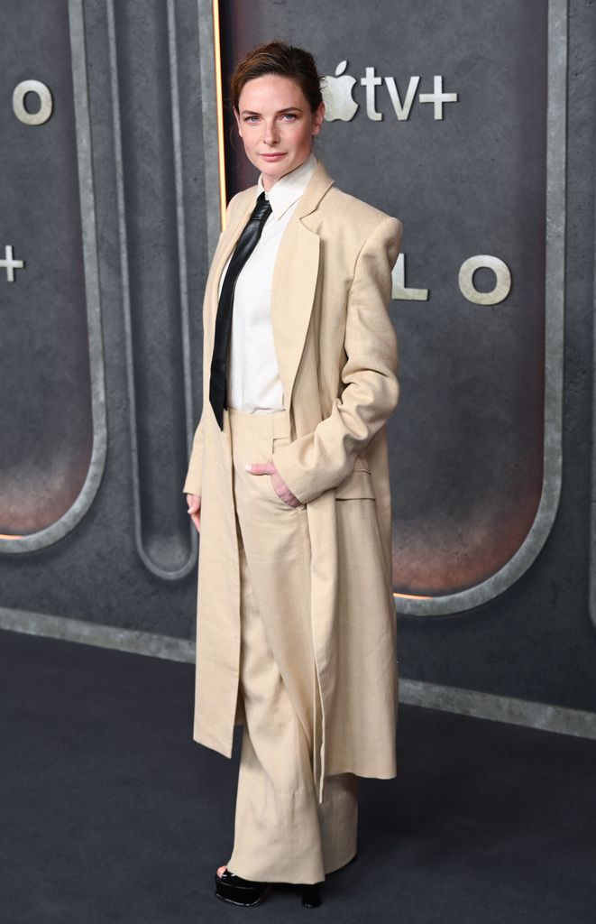 Rebecca opts for an oversized beige suit with a tie and heels at Silo premiere, embodying power-dressing sophistication.