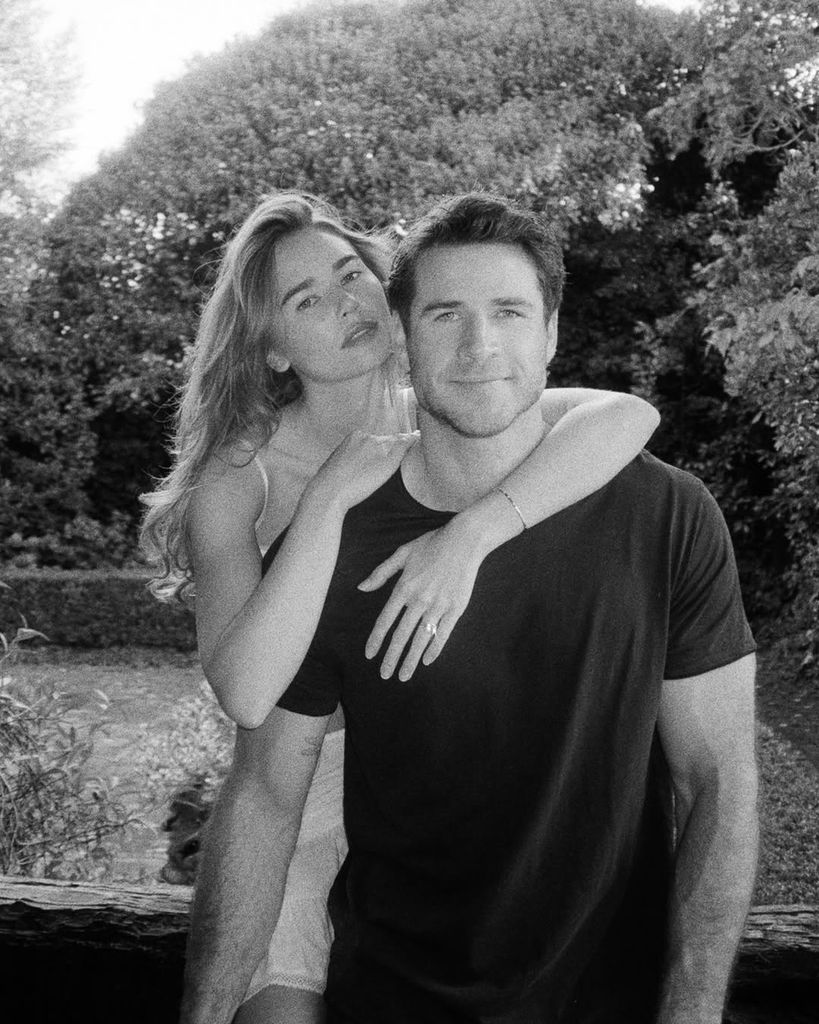Black-and-white photo of Gabriella embracing Liam Hemsworth from behind as they pose for the camera