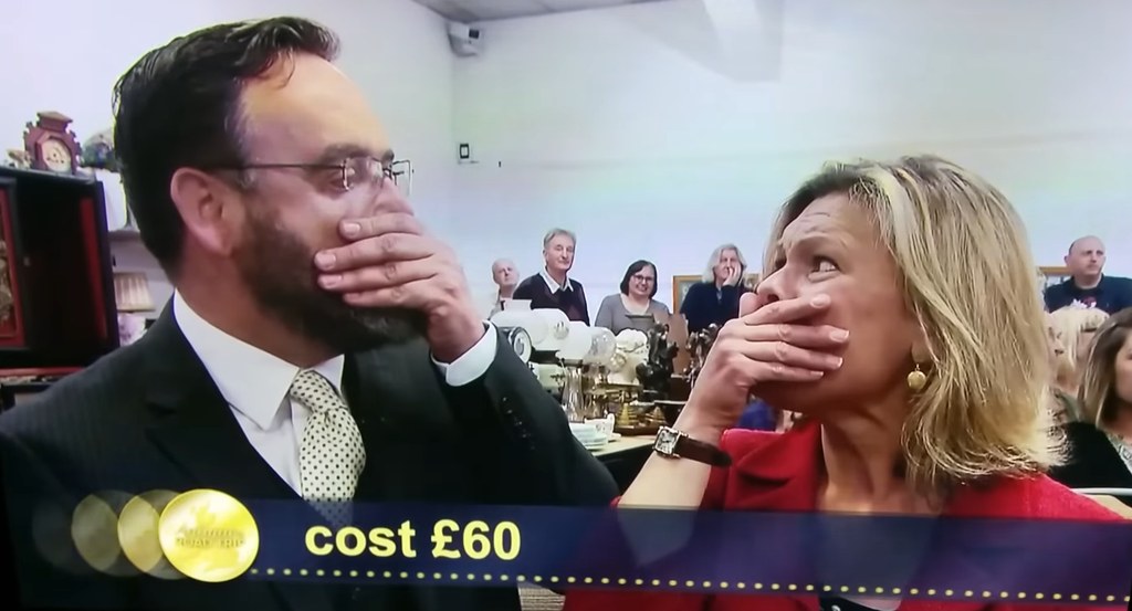 Two people in auction house with hands covering mouths in shock