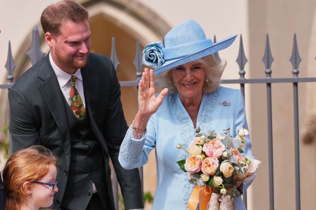 Queen Camilla waving to crowd and holding a posy