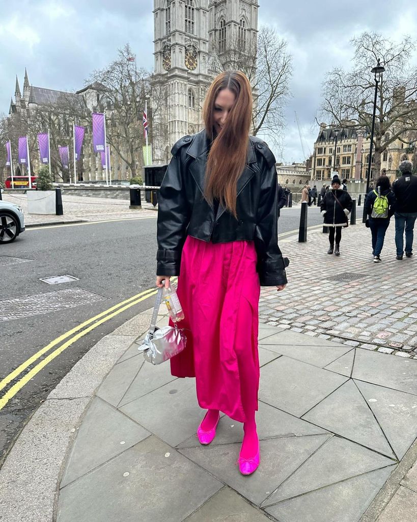 Clare Pennington in a black biker jacket, neon pink midi skirt with matching tights and ballet flats.