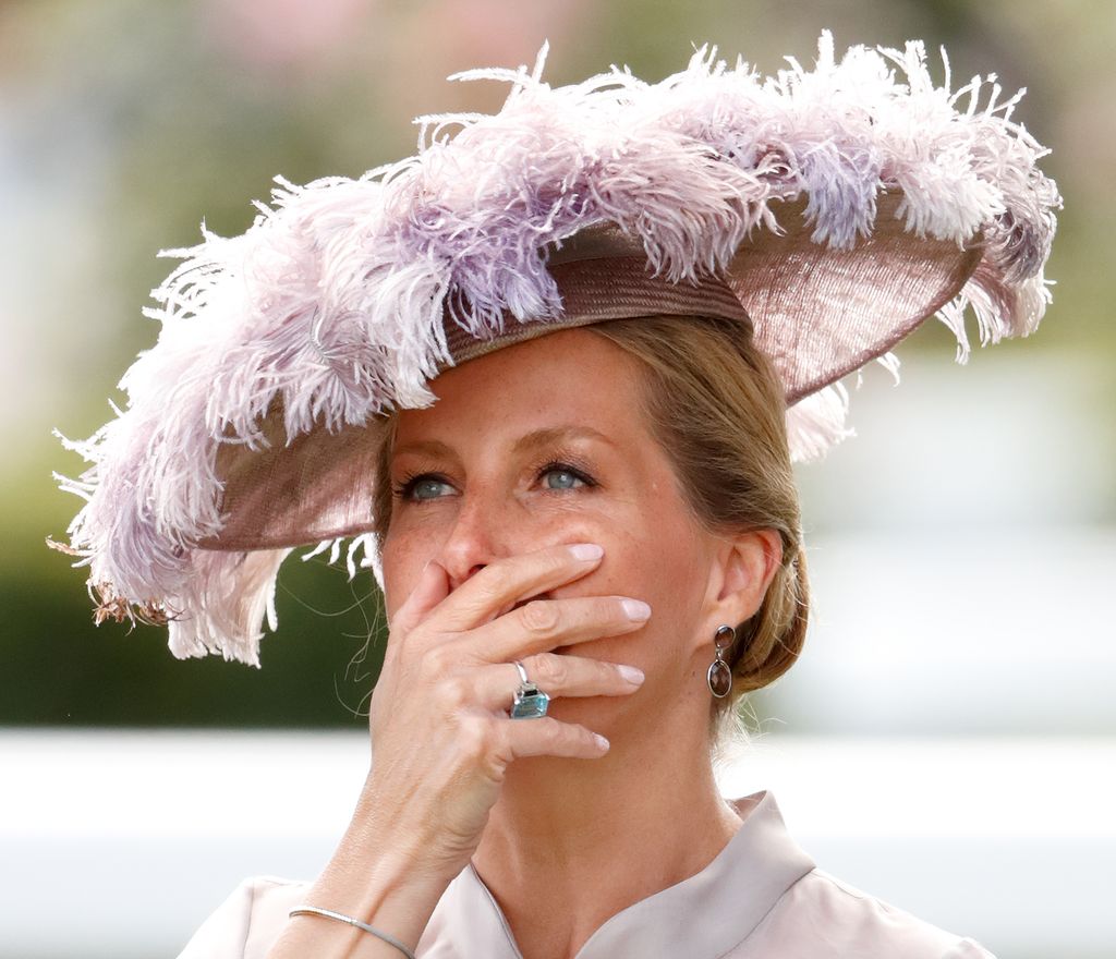 sophie in mauve feathered hat with hand over mouth