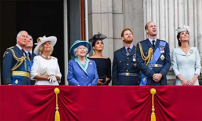 the seninor members of the royal family stand wearing shades of blue on Buckingham Palace balcony as they look up at the sky