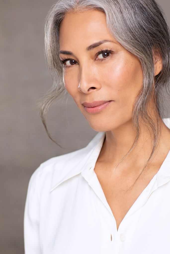Woman with grey hair in a white shirt smiling for the camera