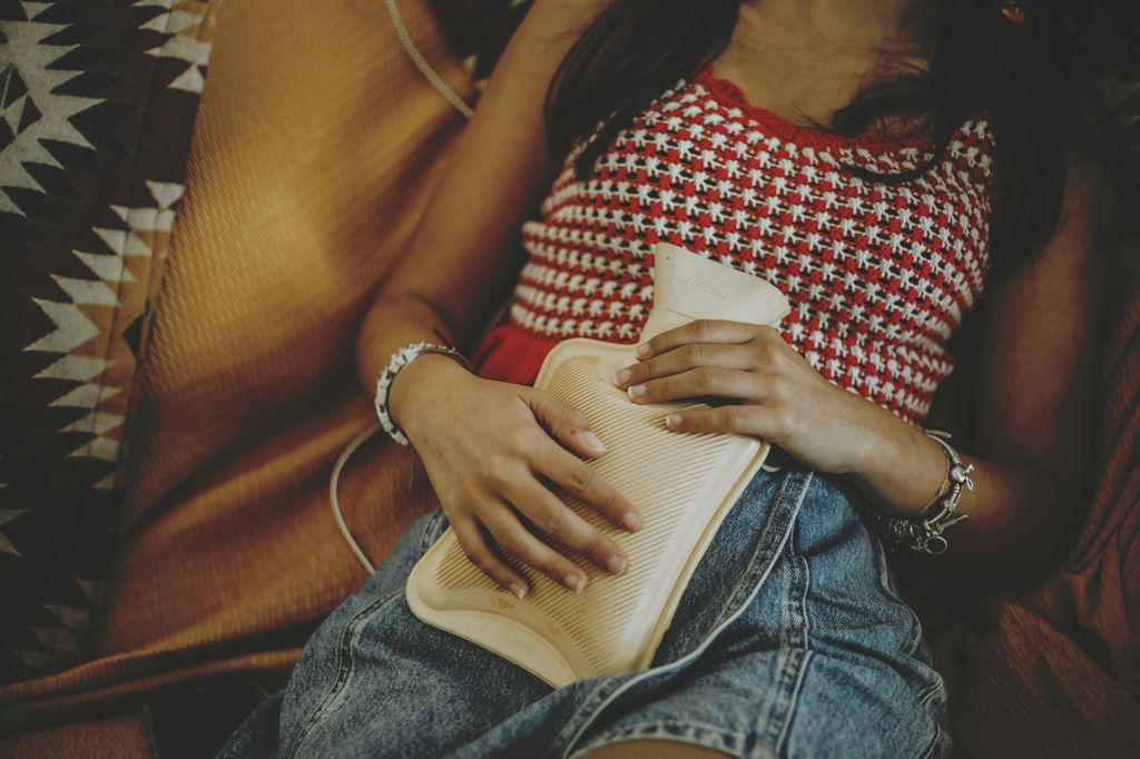 woman in red and white vest and jeans clutching hot water bottle to her stomach