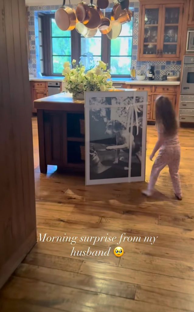 Lilibet in Montecito kitchen looking at framed photo of Meghan and Guy