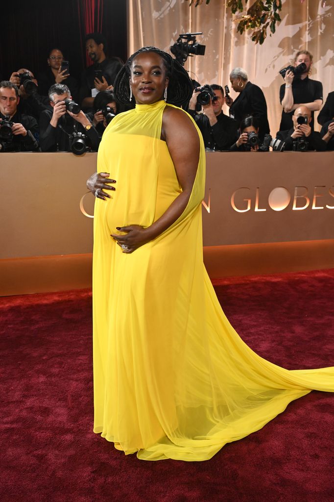 woman wearing yellow dress holding baby bump on red carpet