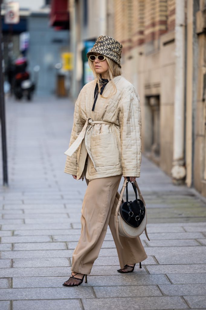 Joicy Muniz wears black bag with heart shape bag, bucket hat, belted jacket, brown pants, net shoes, sunglasses during Paris Fashion Week - Womenswear Fall Winter 2023 2024 : Day Three on March 01, 2023 in Paris, France
