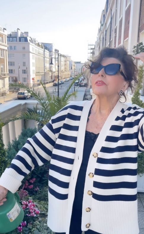 Joan Collins in a breton cardigan while watering plants on a terrace