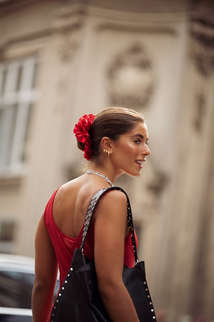  A guest wears long red sheer maxi dress, black bag, silver layered necklaces, red scrunchy for hair outside the Gestuz show during day four of the Copenhagen Fashion Week (CPHFW) SS25 on August 08, 2024 in Copenhagen, Denmark.