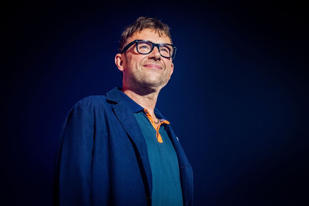 Damon Albarn smiling on stage in blue