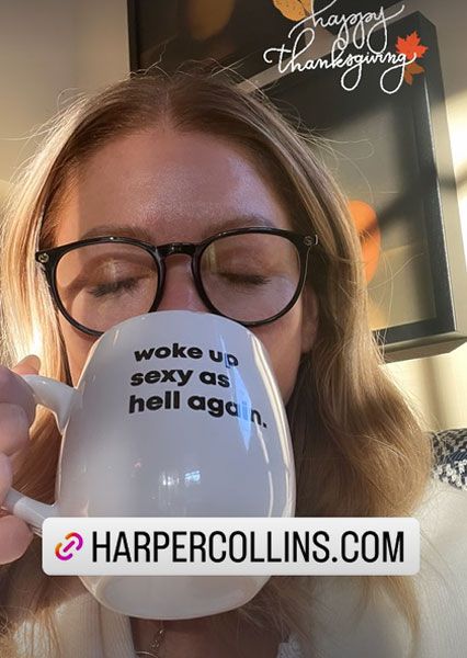 Kelly Ripa drinking from a mug in black glasses