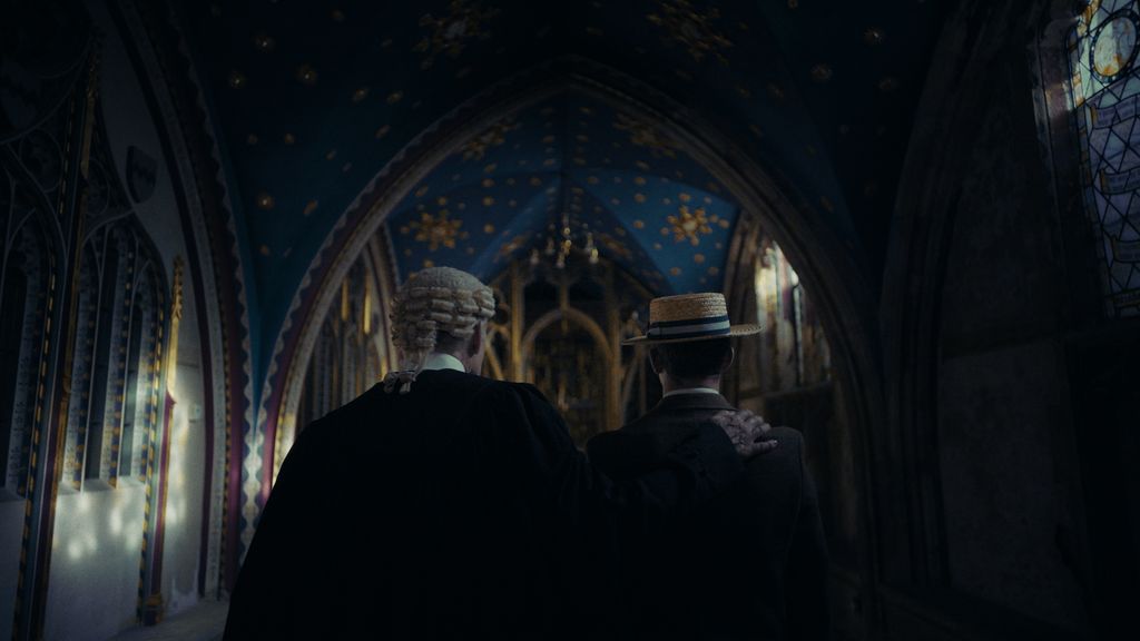 A man in a barrister's wig walking with his arm around a young man