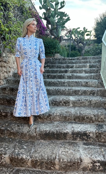 Amelia on steps in white and blue printed midi dress