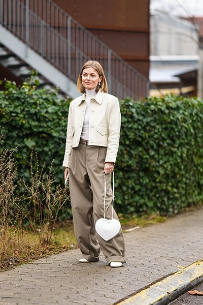 Woman wears cute outfit of cream jacket baggy trousers and white bag