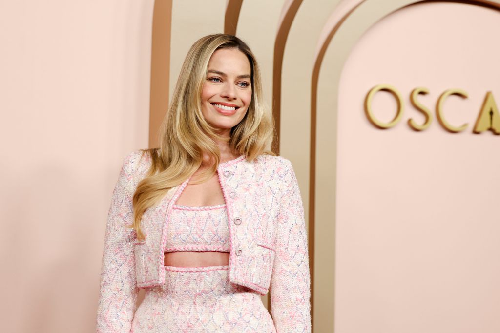 Margot Robbie smiling in a pink jacket and crop top at the Oscars Luncheon