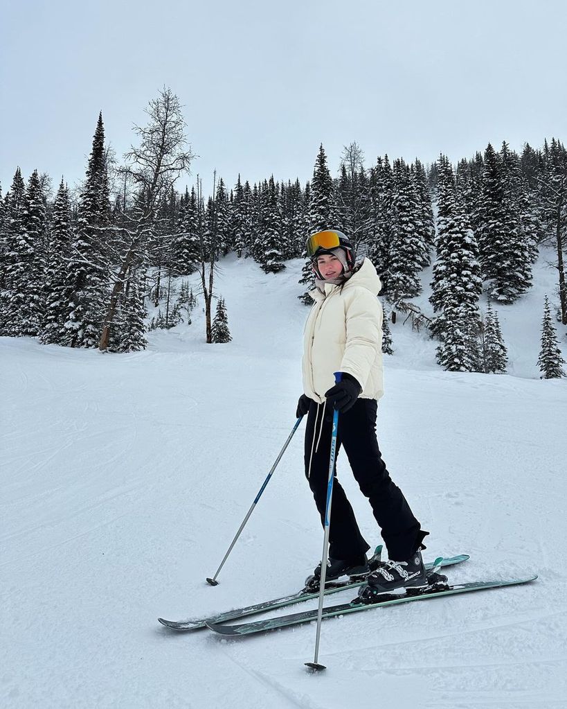 Lily James skiing wearing a white jacket and black trousers