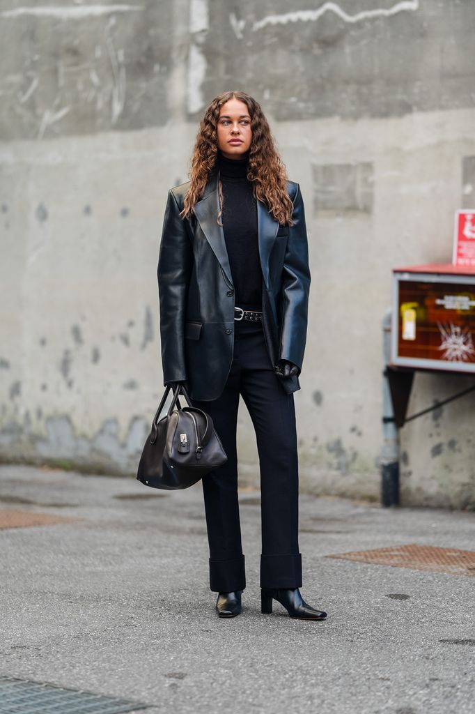 Sarah Lysander wears black turtleneck long sleeve Tod's shirt, shiny black leather jacket, black leather belt, shiny black Tod's leather bag, shiny black heeled leather boots, outside Tod's, during the Milan Fashion Week Spring/Summer 2024-2025 on September 20, 2024 in Milan, Italy.