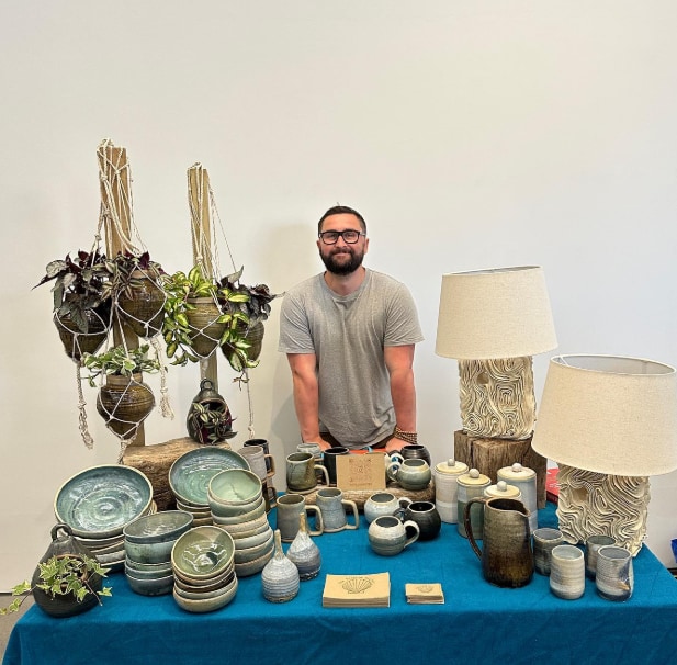 man behind a table of pottery 