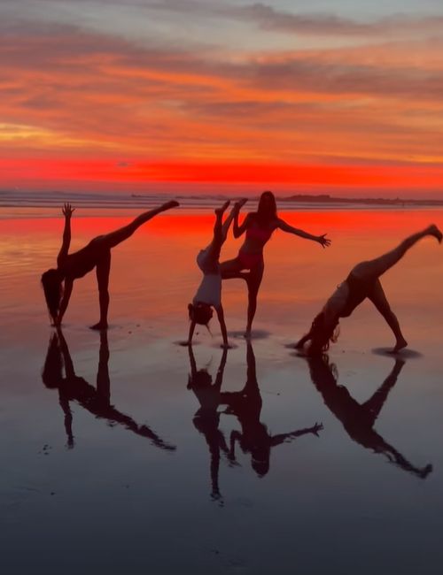 Four women doing yoga poses on the beach