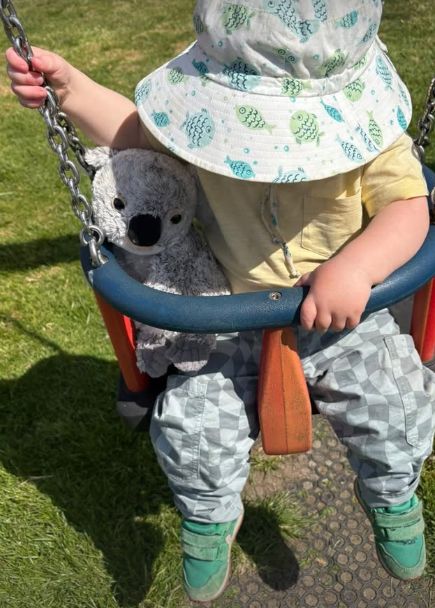 A young boy with a toy koala sitting in a swing