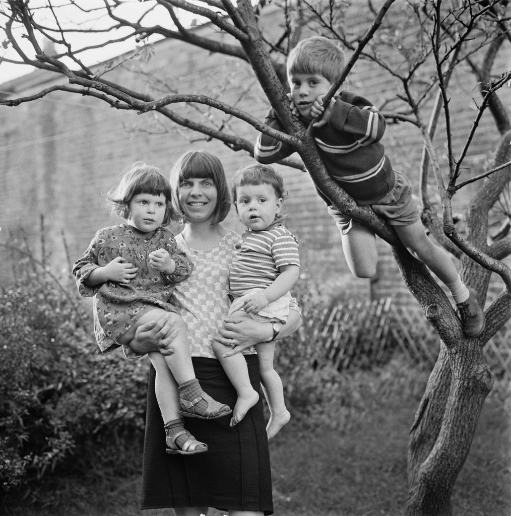 Margaret Drabble tenant deux enfants dans ses bras, avec un jeune garçon grimpant à un arbre