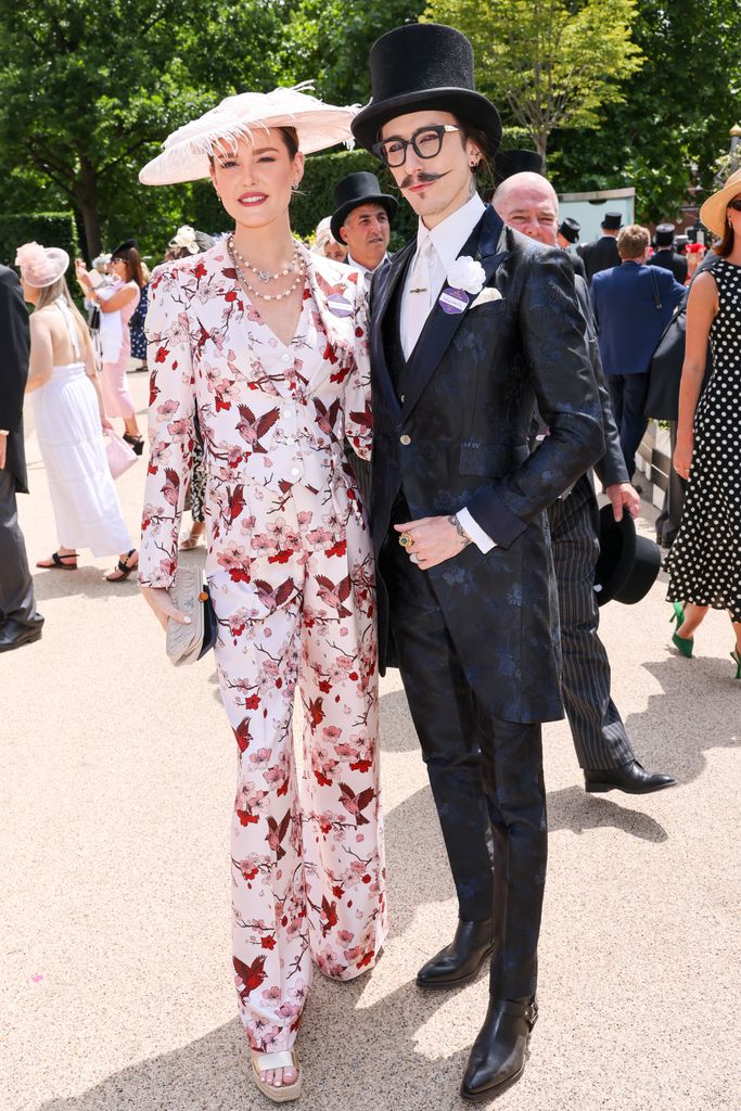 Lottie Archer-Kane and Joshua Kane at Royal Ascot wearing dramatic formalwear: she in a floral suit and he in a jacquard morning coat and top hat.
