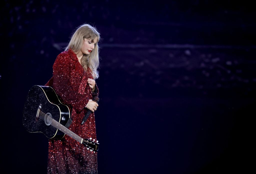 Taylor Swift in a sparkly red coat with a black guitar