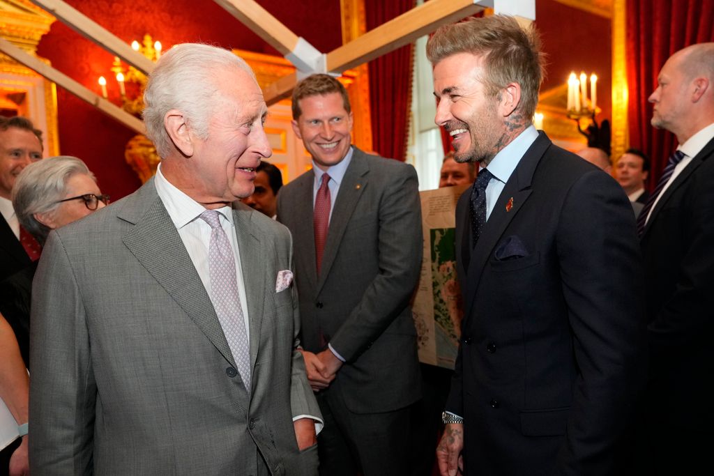 David Beckham laughing with King Charles, both of them dressed in suits 