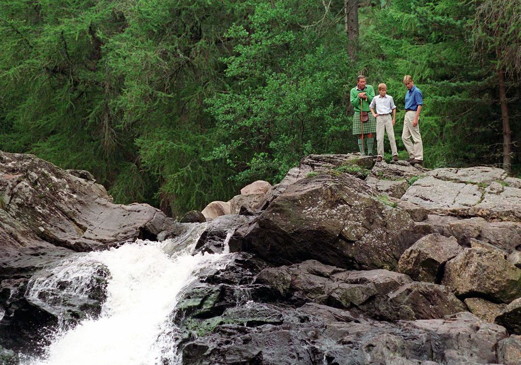 Charles, William And Harry At Balmoral standing on a rock over a waterfall