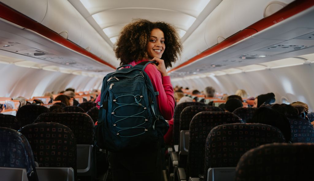 A young woman boards a small commercial airplane, carrying a backpack.