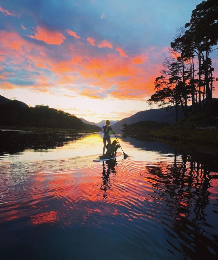 Alizee Thevenet paddleboarding with dogs in Scottish Highlands in front of sunset