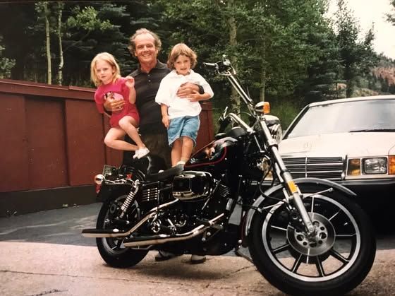 old photo showing Jack Nicholson stood by a motorbike holding up two of his children, Lorraine and Ray when they were children