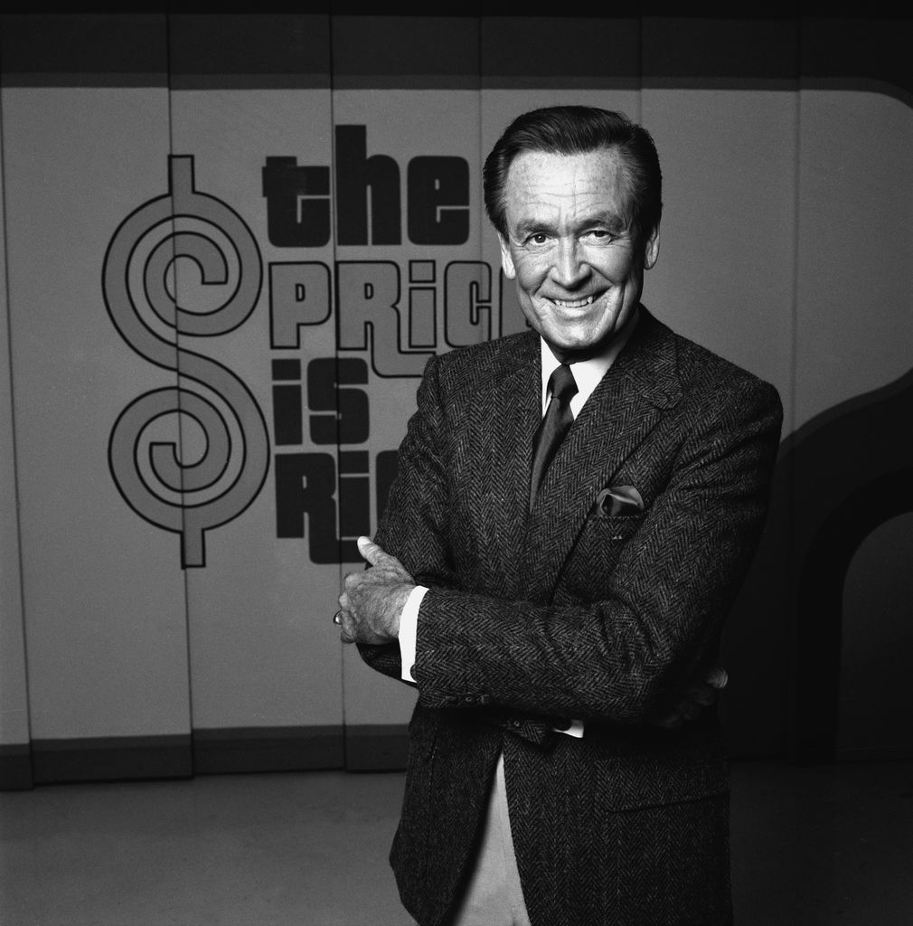 American game show host Bob Barker stands and smiles with arms crossed on the set of his 'The Price is Right,' in 1985